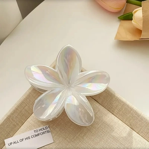 Pince à cheveux fleur de frangipanier blanc perle irisé sur un plateau en osier beige