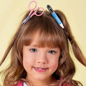 Creative pencil and pink scissor hair clips worn by a young girl with brown hair
