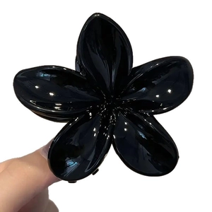 Pince à cheveux fleurie noire brillante pour femme présentée en gros plan tenue à la main