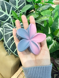 Dettaglio molletta per capelli a fiore sfumato blu e rosa su sfondo di foglie verdi