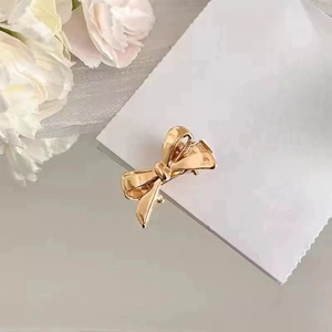 Close-up of golden bow hair clip with high-gloss metallic finish on a white card