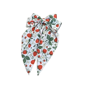 Detail of white bow hair clip featuring strawberry prints and long flowing streamers