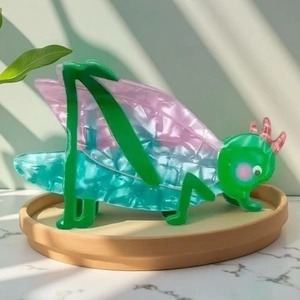 Vibrante grüne Grille Haarklammer mit rosa Flügeln auf einem neutralen Tablett