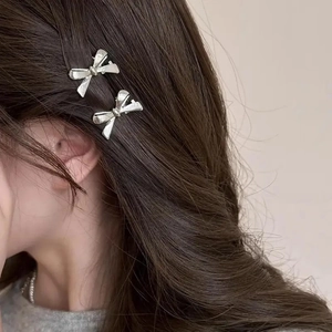 Mini silver bow hair clips with Y2K style on long brown hair, metallic matte finish