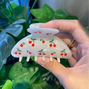 Detail of white acetate hair claw clip with red cherry print held against green plants