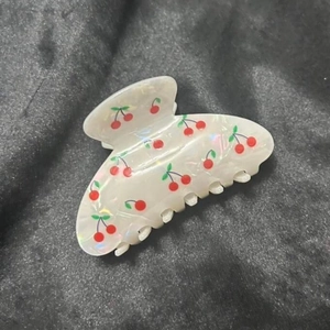 Close-up of cream pearlescent hair claw clip with detailed red cherry print and green leaves