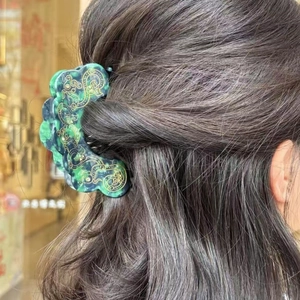 Detail of emerald green marble acetate hair claw with elegant golden floral patterns