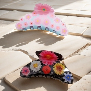 Detailed view of two acrylic floral hair claws on a textured stone surface with shadows