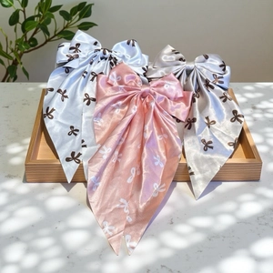 Three elegant satin bow hair clips with mini ribbon prints on a wooden tray