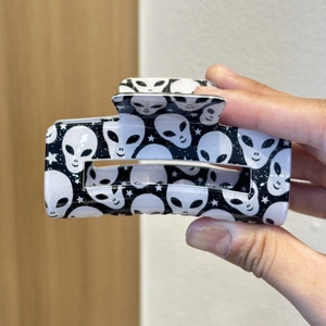 Close-up of a large black hair claw clip featuring white alien head and star prints