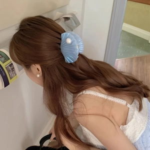 Pinza per capelli a conchiglia blu con perle indossata su lunghi capelli mossi e ricci