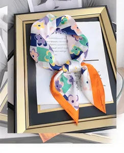 Dettaglio artistico di un foulard in seta con stampa floreale e bordi arancioni vivaci