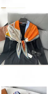 Close-up of diamond silk scarf with orange horse print and geometric stripes on a black sweater