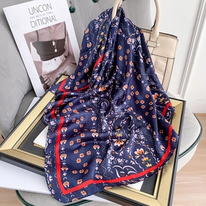Navy floral square silk scarf with orange flowers and red border on a beige handbag