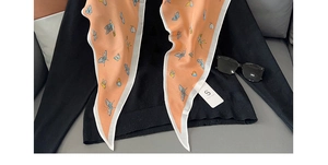 Détail d'un foulard en soie orange avec motif papillon posé sur un pull noir