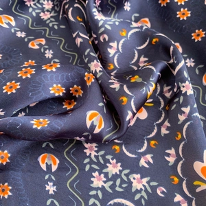 Detail of navy blue silk scarf with orange floral pattern and soft smooth texture