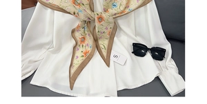 Detail of floral silk scarf with beige tones and brown border on white chiffon shirt