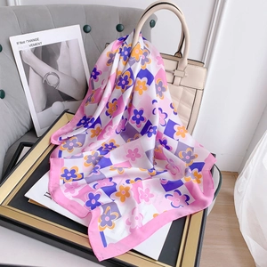 Dettaglio di un foulard in seta floreale con motivi a quadri colorati su una borsa beige