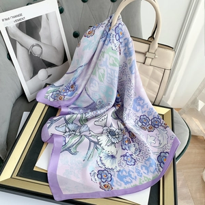 Elegant purple silk scarf with floral pattern draped on a beige handbag with satin borders
