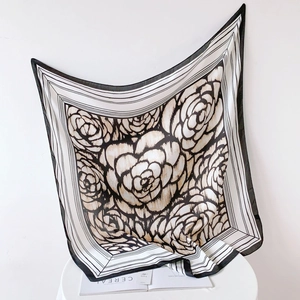 Elegant black and white camellia silk square scarf draped on a white chair