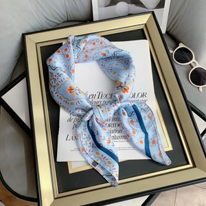 Floral print silk square scarf in light blue with orange flowers on a magazine