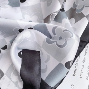Dettaglio di un foulard in seta con motivo a scacchi e fiori con raffinati bordi arrotolati
