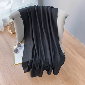 Close-up of lightweight black cotton linen shawl draped on a chair with summer accessories