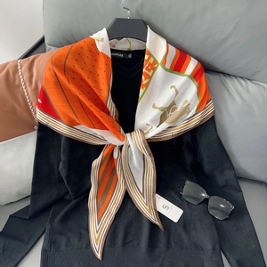 Detail of an orange horse-themed silk scarf styled over a black V-neck sweater on a sofa