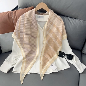 Détail d'un foulard en soie à carreaux beige avec une chemise blanche sur un canapé