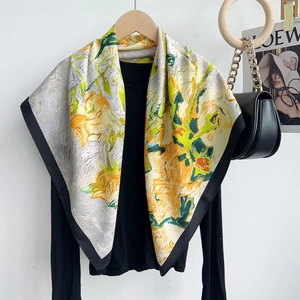 Artistic floral square silk scarf in yellow and green tones draped on a hanger