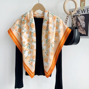 Détail d'un grand foulard soyeux avec imprimés floraux oranges sur un cintre en bois
