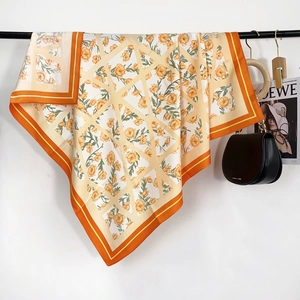 Gros plan d'un foulard en soie à fleurs avec bordures oranges sur un cintre élégant
