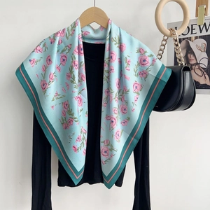 Détail d'un foulard en soie bleu clair avec imprimé floral rose et bordures contrastées