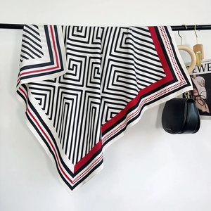 Détail d'un foulard effet soie avec motifs géométriques noirs et blancs et bords rouges