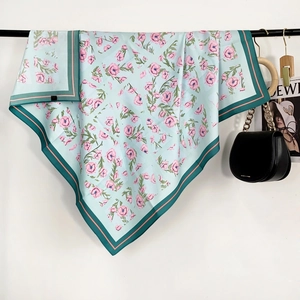 Détail d'un foulard en soie vert menthe avec imprimés floraux roses et bordures