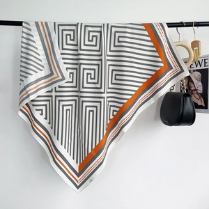 Détail d'un foulard en soie avec motifs grecs gris et bordures orange contrastées