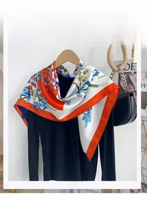 Close-up of elegant floral print square scarf with orange borders on a black garment