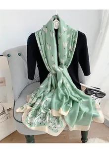 Detail view of a light green silk-like scarf with white floral print on a chair