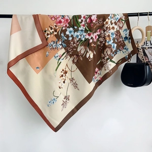 Detail of silk-feel floral square scarf in warm tones draped elegantly with a handbag
