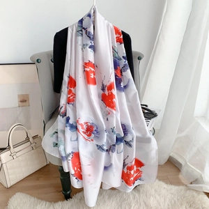 Elegante sciarpa di seta bianca con motivi floreali rossi e blu su una poltrona moderna