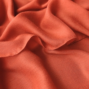 Detail of brick red cotton linen scarf showing soft grain texture and draped fabric folds
