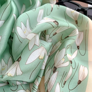 Detail of light green silk-like scarf featuring elegant white lily floral patterns