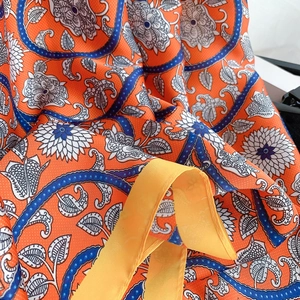Macro shot of orange floral paisley silk-like fabric with premium stitched hem details