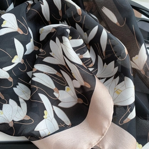 Detailed close-up of green floral silk scarf with magnolia prints and satin borders