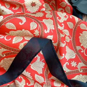 Close-up of red floral silk scarf fabric with elegant black translucent lace edge detailing