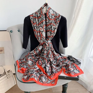 Floral print silk scarf with red border displayed on casual sofa with fashion accessories
