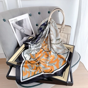 Elegant silk scarf with orange and blue botanical print draped on a stylish beige handbag