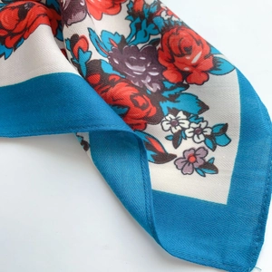 Detailed view of floral silk scarf with red roses and blue edges in twill texture