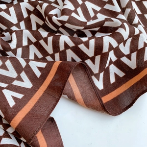 Detail of soft twill scarf featuring brown V-pattern monogram and orange border trim