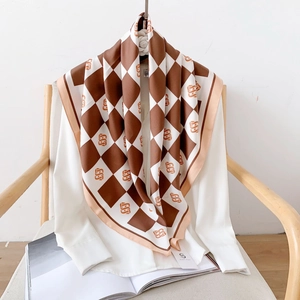 Brown and white checkered satin scarf with S logo draped on a white shirt and chair